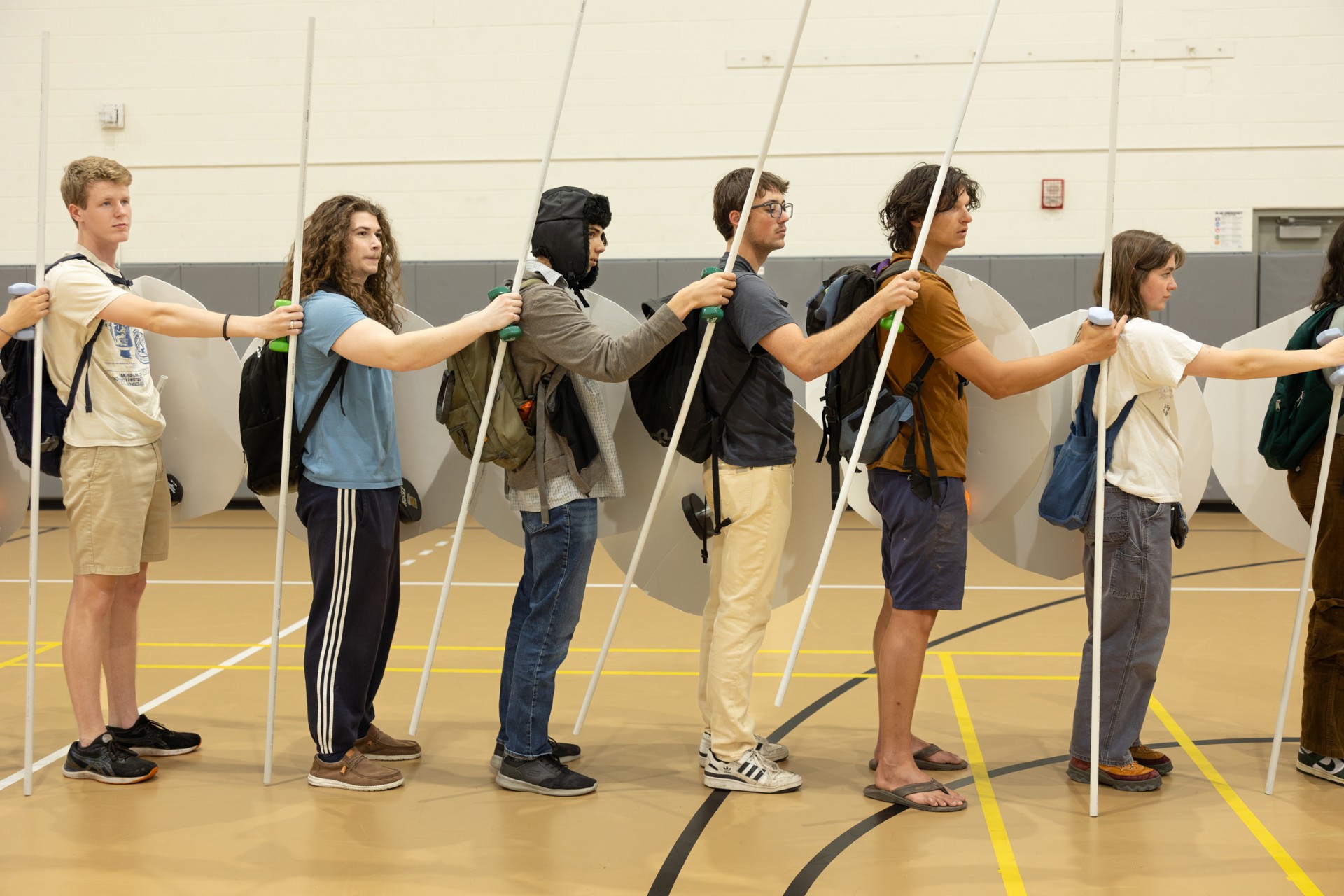 Students from the 2024 class simulate being hoplites by wearing one backpack in front and one in back, as well as a helmet, and then using cardboard silhouettes of a hoplite’s shield and of his weapons, which were cut PVC pipe segments. Students filled their backpacks, pockets, and hands with weights that accurately simulated the weight of various pieces of gear, including armor, shield, spear, and sword. Photo by Eileen Broderick.
